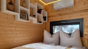 A wooden-paneled room with a bed, shelves with books, and a window with a view of trees.