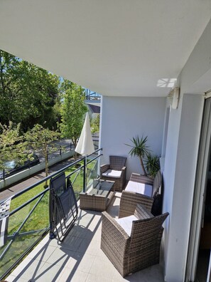A balcony with wicker furniture, a glass table, and a potted plant.