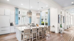 Una cocina amplia con una isla grande, armarios blancos y cortinas azules a cuadros.