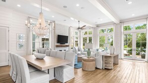 Un salón amplio con una mesa de comedor de madera, sofás blancos y una lámpara de araña.