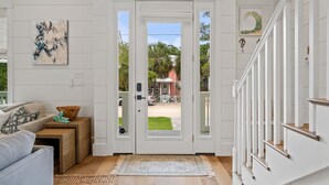 Un interior blanc amb una porta que diu "SEAGROVE BEACH", una taula auxiliar de vimet, un sofà gris i una escala.