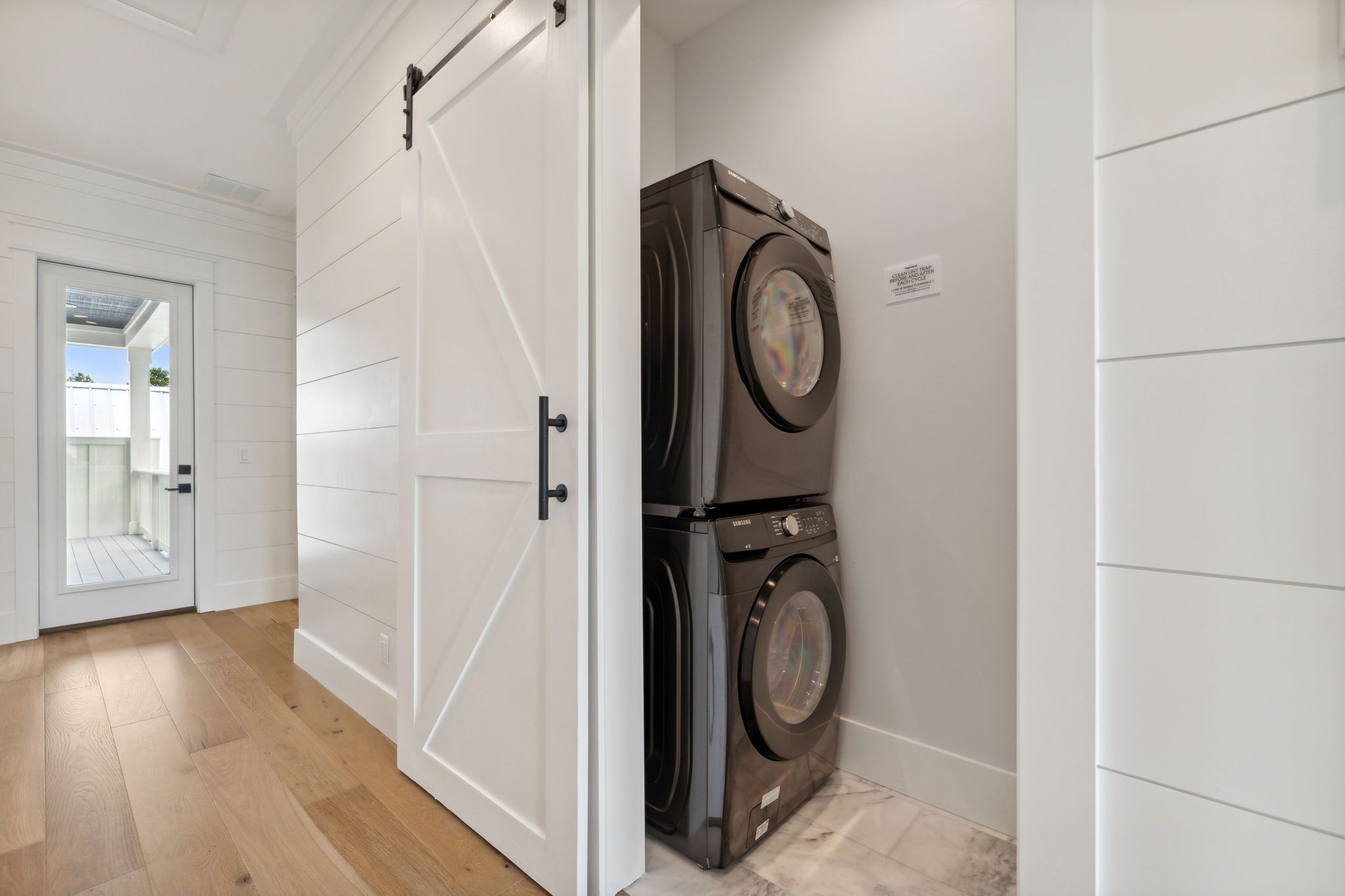 A laundry room with a front-loading washer and dryer, white walls, and a wooden floor.