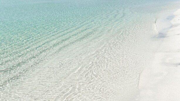 Una platja amb aigua turquesa cristal·lina i sorra blanca.