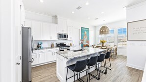A modern kitchen with white cabinetry, a central island with bar stools, and a dining area with a view. - *SPECIAL* Summer Salt 38*NEW* SLEEPS 19 4 bed 4.5 bath home Orange Beach (Orange Beach)