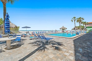 A pool area with lounge chairs, umbrellas, and a view of the ocean.