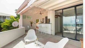 Ein moderner Außenbereich mit Terrasse, weißem Mobiliar, einer Bar und einer Glastür, die auf einen Balkon führt.
