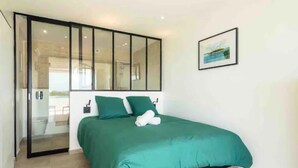 Ein Schlafzimmer mit einem Bett, einer grünen Bettdecke, zwei Kissen, einem gerahmten Bild an der Wand und einer Schiebetür zu einem Balkon.