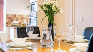 A dining table set with plates, glasses, and a pitcher of water, with a vase of flowers in the background.