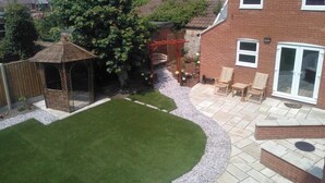 A residential backyard with a patio, a wooden pergola, a small shed, and a lawn.