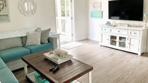 A living room with a teal sofa, a wooden coffee table, a white cabinet, and a television on the wall. - HeartWind Cottage -Quaint and cozy with private pool, steps to the beach (Santa Rosa Beach)
