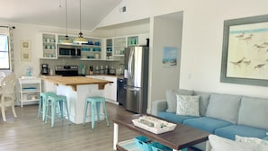 A modern kitchen with white cabinets, a central island, and blue stools. - HeartWind Cottage -Quaint and cozy with private pool, steps to the beach (Santa Rosa Beach)
