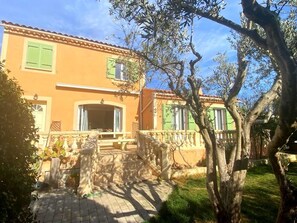 A two-story building with a tiled roof, green shutters, and a stone staircase leading to the entrance.