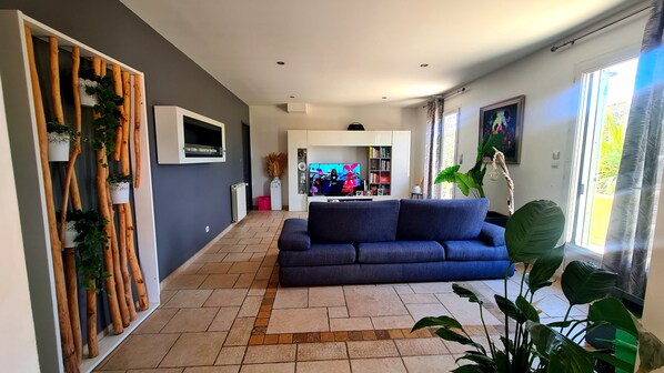 A living room with a dark blue sofa, a television, and a large window with curtains.