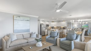 Una sala de estar moderna con un sofá, sillones y una mesa de centro. Se ve una cocina al fondo con una zona de comedor.