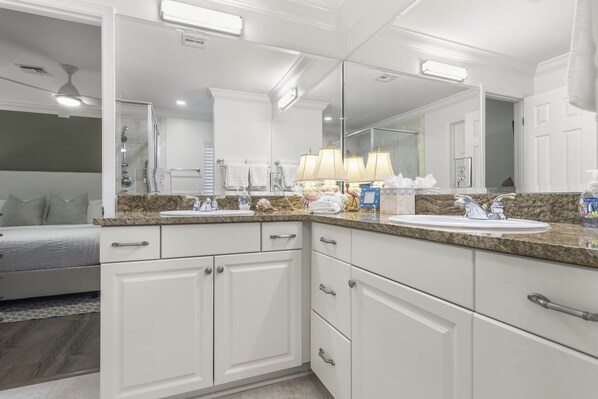 A modern bathroom with a large mirror, white cabinetry, a granite countertop, and a shower area.