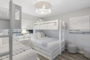 A modern bedroom with a bunk bed, a bedside table with a lamp, a large window, and a framed picture on the wall.