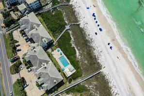 An aerial view of a coastal property with a swimming pool, beach access, and multiple buildings with sloped roofs.