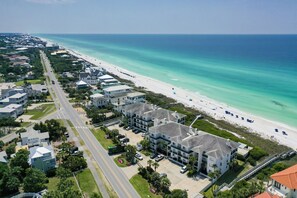 An aerial view of a coastal residential area with beachfront properties, a main road, and a beach with umbrellas.