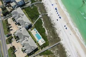 Vue aérienne d’une propriété située sur la côte, dotée d’une piscine, d’un accès à la plage et de plusieurs bâtiments aux toits inclinés.