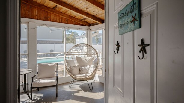 A covered outdoor seating area with a wicker chair, a small table, and a view of a pool.