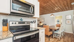 A modern kitchen with white cabinetry, a stainless steel oven, and a wooden ceiling.