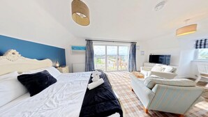A hotel room with a bed, a sofa, a TV, and a balcony with curtains.