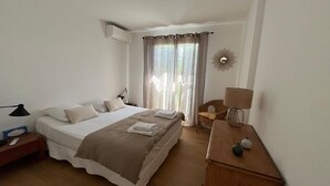 A hotel room with a bed, bedside table, lamp, chair, and a window with curtains.