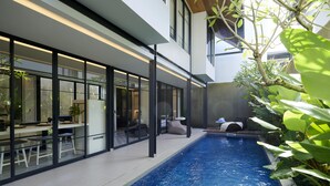 A modern indoor pool area with glass walls, seating, and a view of the pool. - Adamare Villa Umalas (Kerobokan)