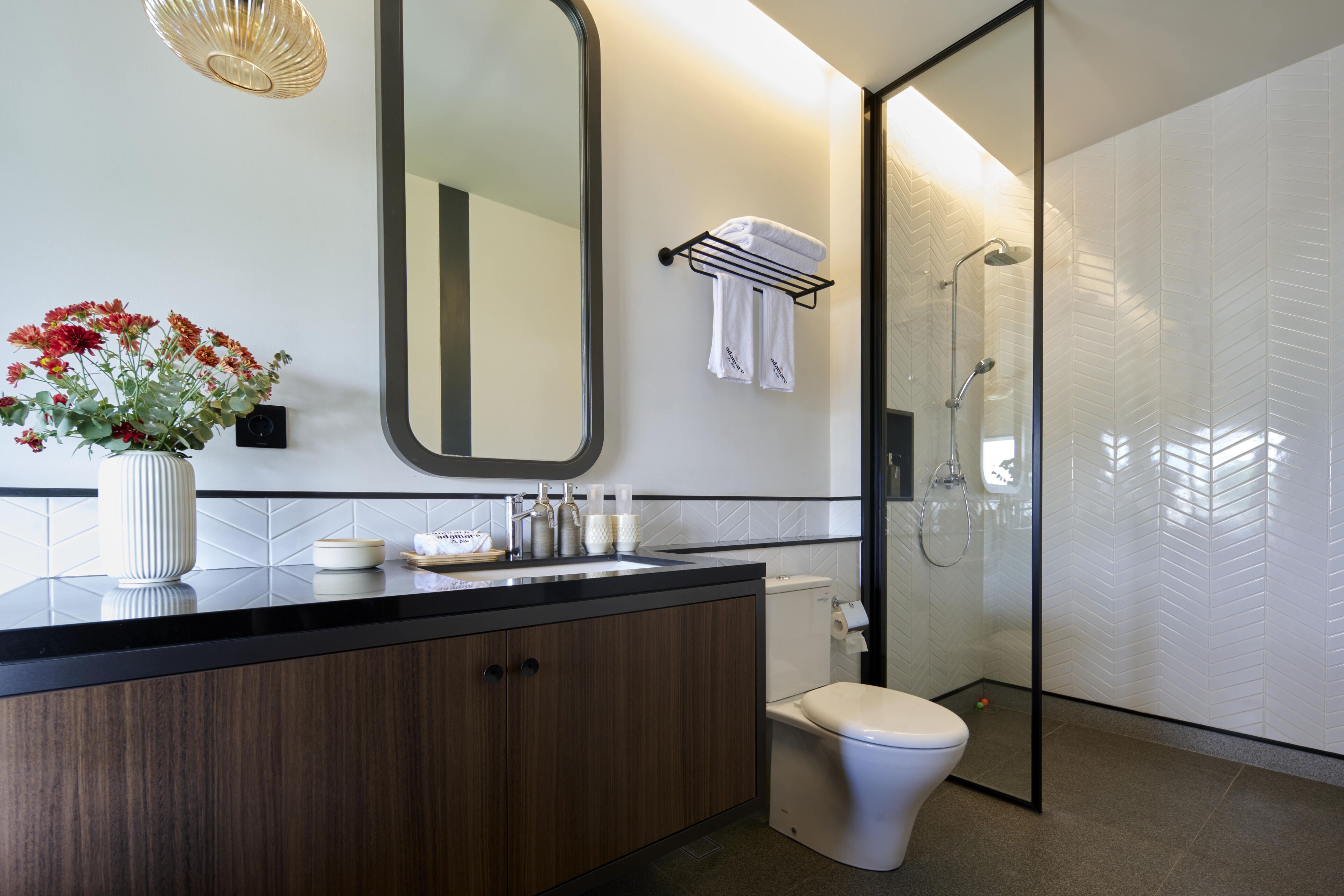 Et moderne badeværelse med en trækommode, toilet, glasvæg ved brusebad og et stort spejl.