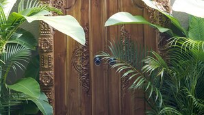 A wooden door with intricate carvings and a metal handle, surrounded by lush green plants. - Adamare Villa Umalas (Kerobokan)