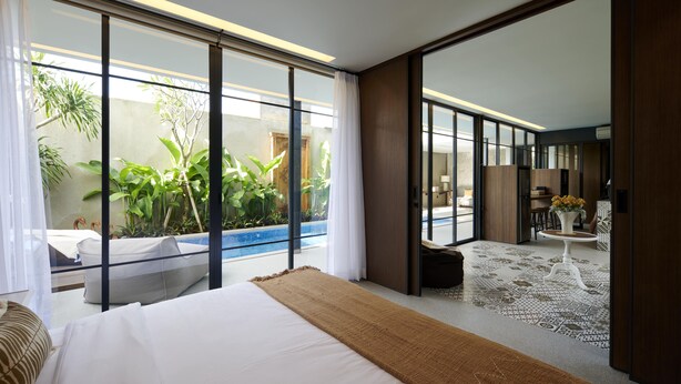 A modern hotel room with a large bed, a small pool, and a view of greenery outside. - Adamare Villa Umalas (Kerobokan)