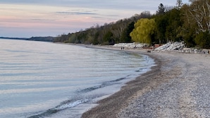 Una playa con orilla de guijarros, árboles y mar tranquilo.