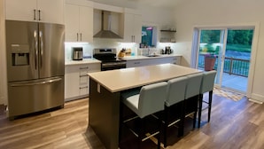 Una cocina moderna con un refrigerador de acero inoxidable, una isla con taburetes de bar y vistas al exterior a través de una puerta corrediza de vidrio.