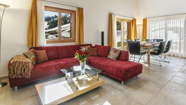 A modern living room with a red sectional sofa, a glass coffee table, and a dining area with a table and chairs. - Martens by Interhome (Les Crosets)