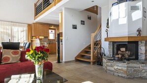 A spacious living area with a glass coffee table, a red sofa, and a vase of flowers. A staircase leads to an upper level with a wooden railing. - Martens by Interhome (Les Crosets)