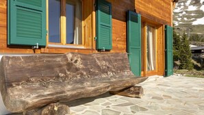 A wooden cabin with green shutters, a stone-tiled patio, and a large log bench. - Martens by Interhome (Les Crosets)
