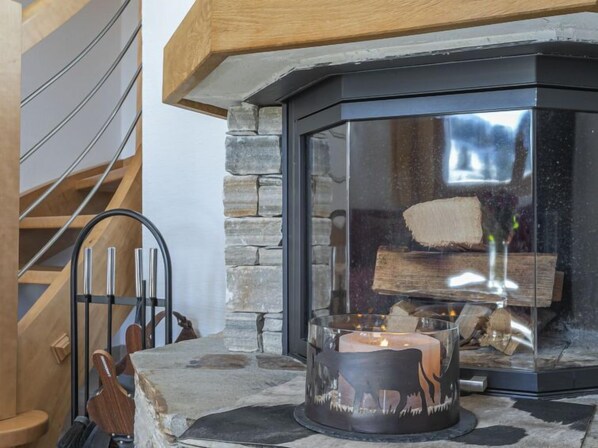 A stone fireplace with a glass enclosure, a candle, and a log fire inside.