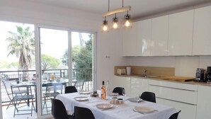 Ein Essbereich mit einem Tisch für vier Personen, eine Küche mit weißen Schränken und ein Balkon mit Blick auf Palmen.