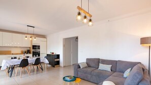 Ein modernes Wohnzimmer mit einem grauen Sofa, einem Esstisch mit Stühlen und einer Küche im Hintergrund.