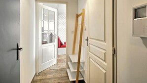 A narrow hallway with a wooden ladder leaning against a white door, a red chair in the background, and a white wall with a window. - Charme de Villès Martin by Interhome (Saint Nazaire)