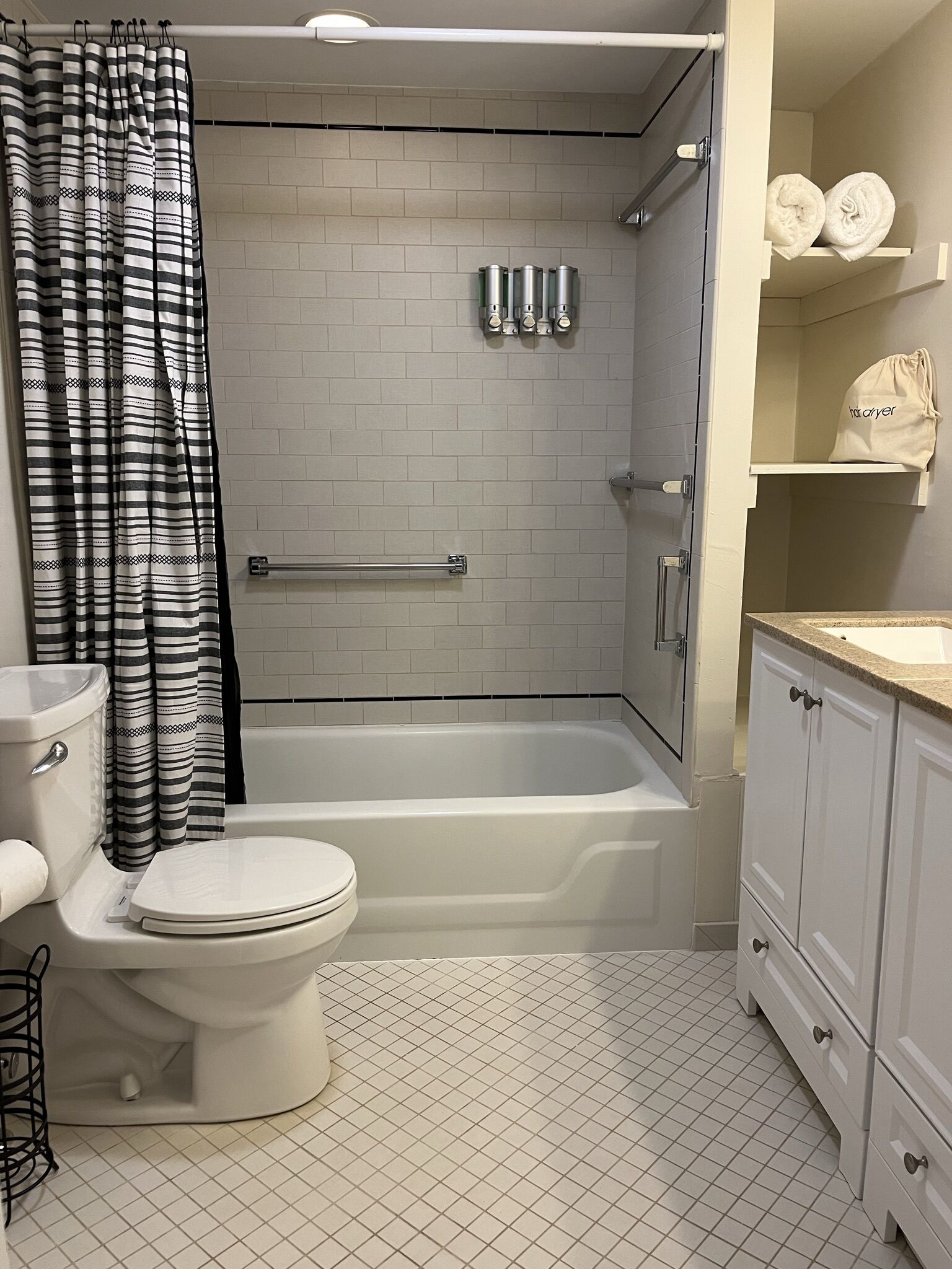 A bathroom with a white toilet, a bathtub, a shower, and a sink. There are towels on the shelf and a bag on the counter.