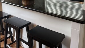 Moderni keittiö, jossa on musta työtaso, ruostumattomasta teräksestä valmistetut kodinkoneet ja ikkuna, jossa on sälekaihtimet.