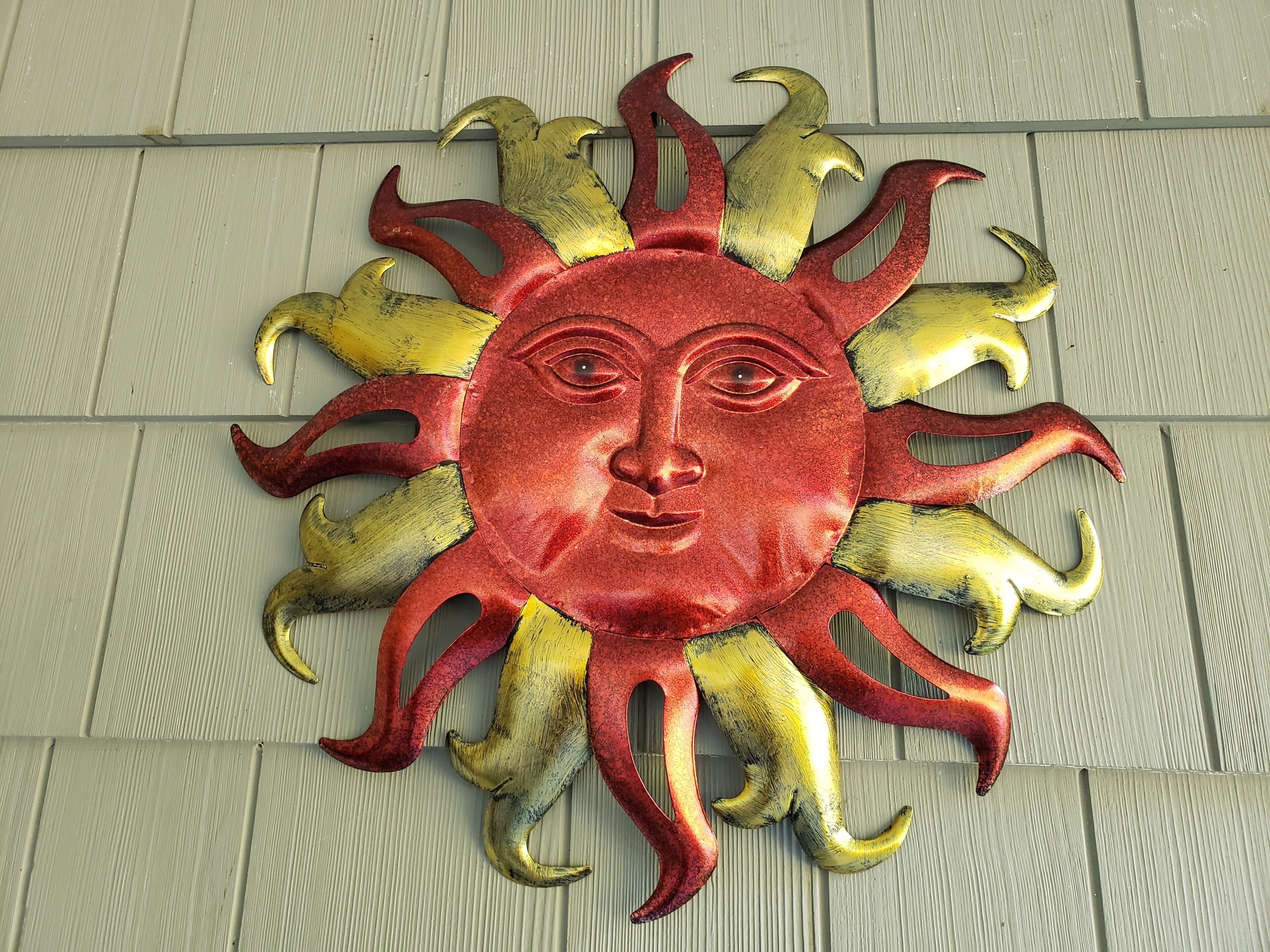 A decorative sun with a face, featuring a red and gold color scheme, mounted on a wall.