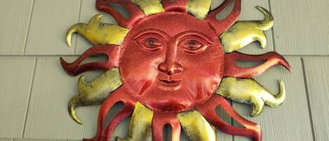 A decorative sun with a face, featuring a red and gold color scheme, mounted on a wall.