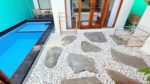 A swimming pool with a stone pathway leading to a glass door entrance. - Villa giyor (Lembongan Island)