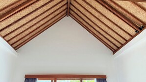 A room with a high ceiling, wooden beams, a large window with curtains, and a view of greenery outside. - Villa giyor (Lembongan Island)