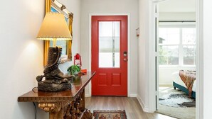 Un pasillo con una consola de madera, una puerta roja y vistas a un balcón.