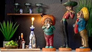 Un comedor con sillas de mimbre, una mesa y una estantería con libros y objetos decorativos.