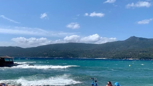 Un paysage côtier avec un ciel dégagé, un bateau et une montagne en arrière-plan.