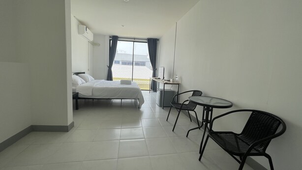 Habitación de hotel con cama, escritorio, dos sillas y un ventanal con cortinas.